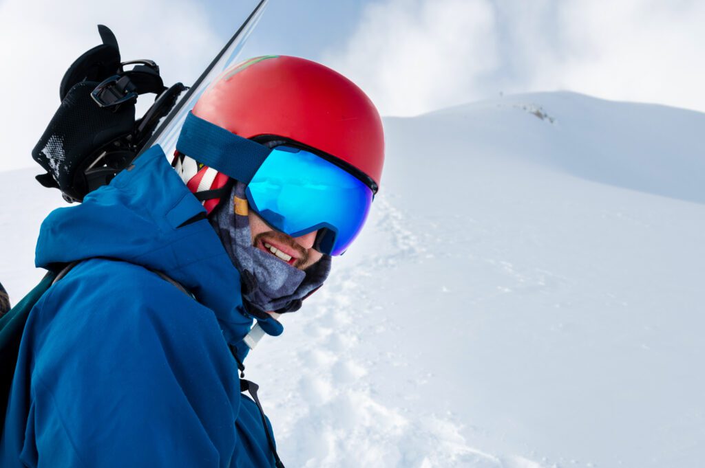 Central Sport man on a hill with snowboard wearing googles and red helmet.