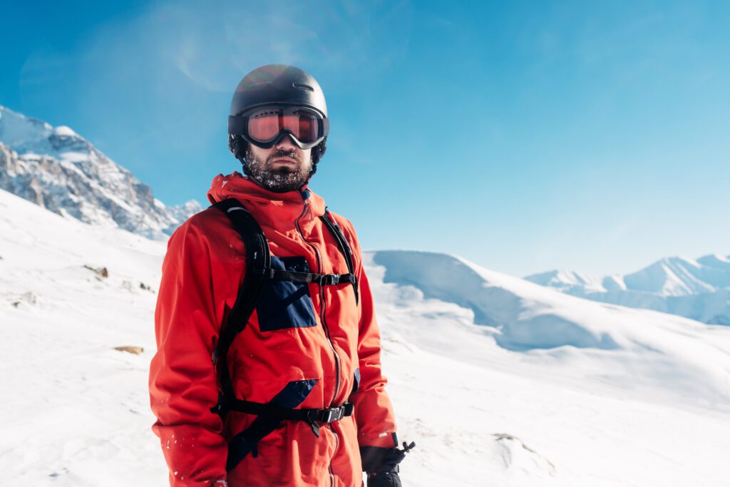 Central Sport - Man standing on a mountain wearing an orange jacket, helmet, and goggles.